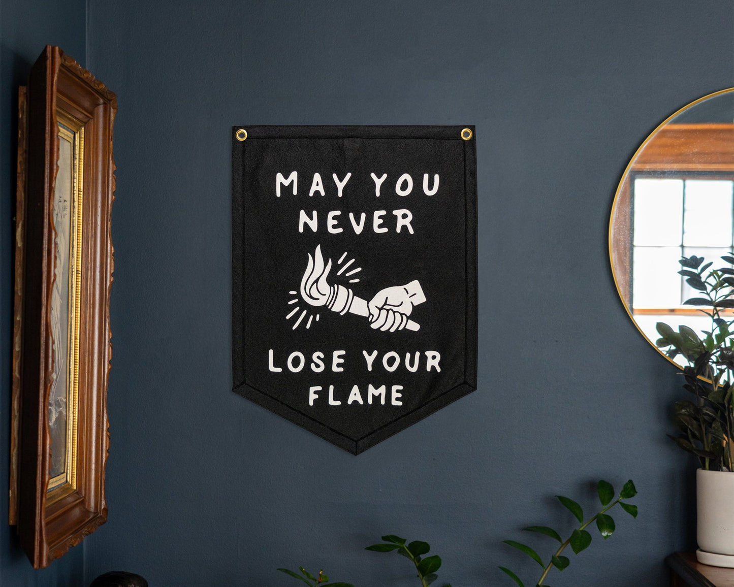 Decorative sign with motivational quote on a dark wall in a room with plants and a bar cart.